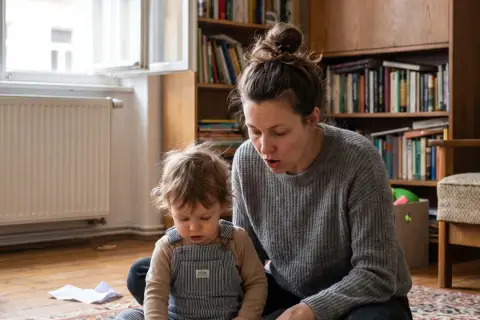 Mama czyta dziecku, wspierając jego pierwsze słowa. W tle regał z książkami.