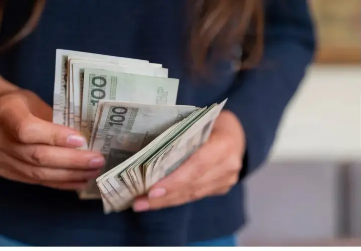 Ręce trzymające stos banknotów 100 zł. Dowiedz się, jak zalatwic płatny urlop wychowawczy i zapewnić sobie wsparcie finansowe.